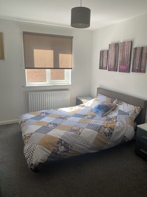 Un dormitorio con cama, una ventana con persianas, un radiador, una mesita de noche y decoración en la pared.