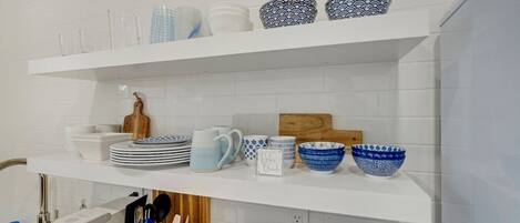 A kitchen with white shelves holding various dishes and utensils.