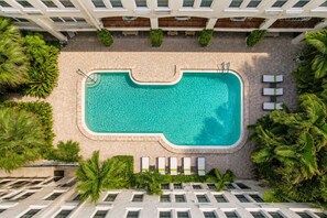 Une piscine sur le toit, avec une fontaine à eau d’un bleu cristallin, entourée de palmiers et de chaises longues.