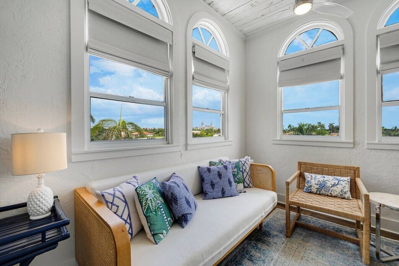 A room with a sofa and a chair, a lamp, and a view through large windows.