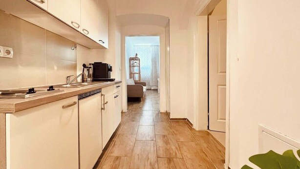 Eine schmale Küche mit Holzarbeitsplatte und -schränken, die in einen Wohnbereich mit Sofa und Fenster übergeht.