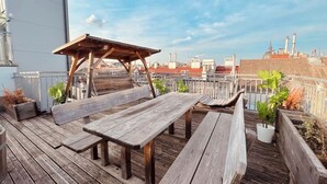 Eine Dachterrasse mit Holzbänken und einer Pergola, umgeben von Topfpflanzen.