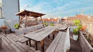 Eine Dachterrasse mit Holzbänken und einer Pergola, umgeben von Topfpflanzen.