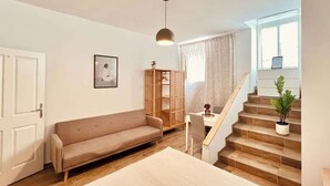Ein Zimmer mit einer Couch, einem Schreibtisch, einer Pendelleuchte, einer Treppe und einem Fenster.