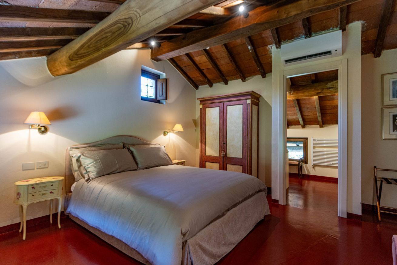 Une chambre avec un grand lit, des poutres en bois, une armoire et une fenêtre.