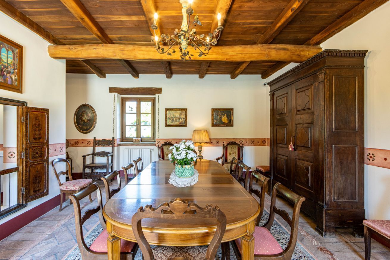 Een eetkamer met een houten tafel, stoelen en een kroonluchter. Er hangen ingelijste foto's aan de muur en staat een grote houten kast.