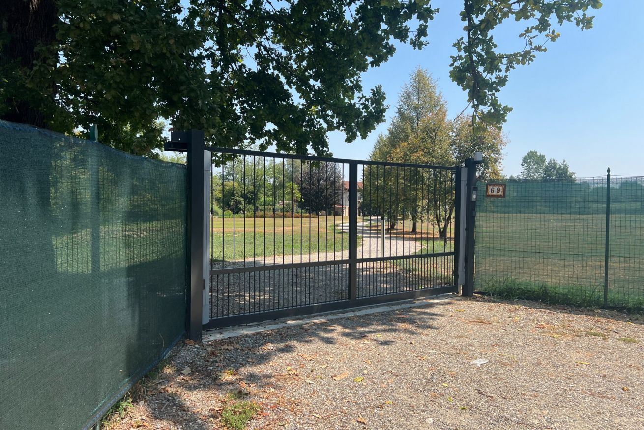 A gated entrance with a metal fence, a grassy area beyond, and a clear sky.