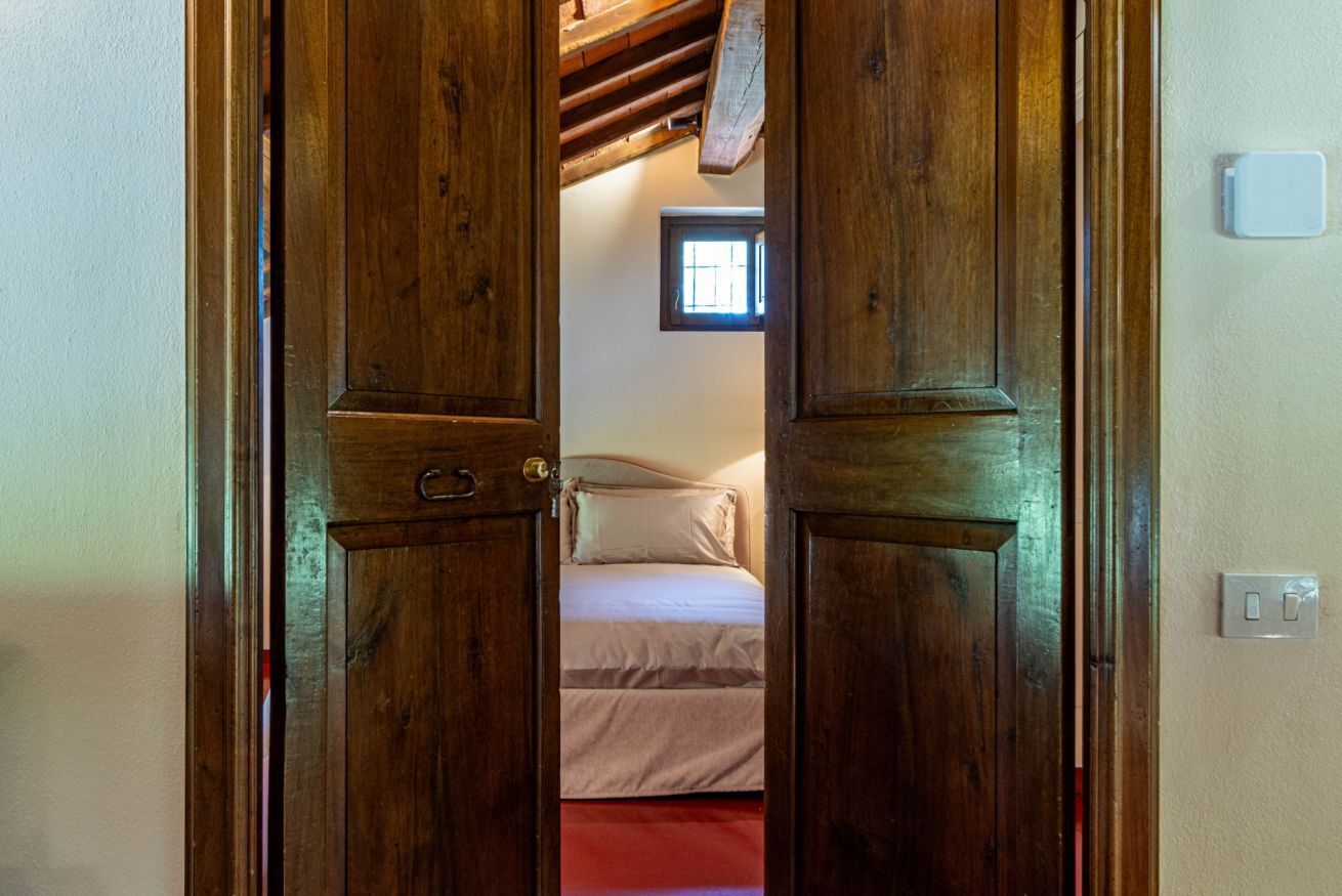 Een houten deur die leidt naar een slaapkamer met een bed en een raam.