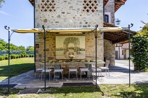 An outdoor dining area with stone walls, a mural, and a covered table with chairs. - Benvenuti a Villa Harmonia, una splendida dimora d’epoca sapientemente restaurata che conserva tutto il fascino autentico delle antiche cascine piemontesi, unendo eleganza, comfort e atmosfera senza tempo.Immersa in oltre 10.000 mq di parco privato, Vi (Dormelletto)