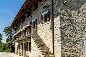Un edificio de piedra con un balcón, contraventanas de madera y una escalera que conduce a la entrada.