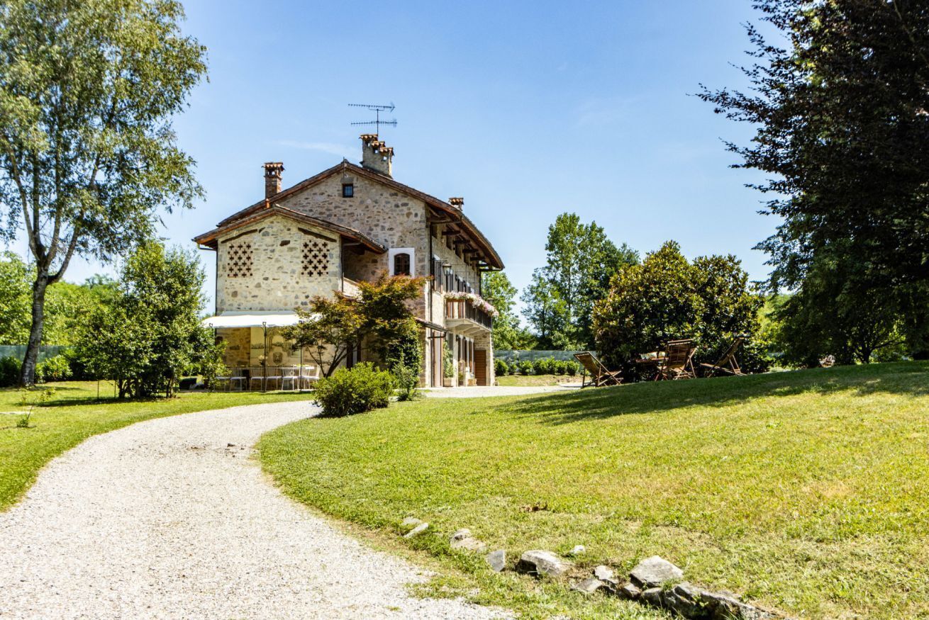 A stone house with a gravel path leading to it, surrounded by greenery.