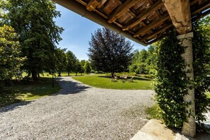 Un sendero de grava que lleva a una pérgola de madera con sillas, rodeada de árboles y un área verde.