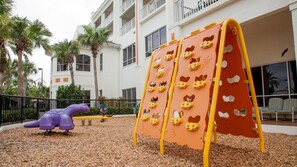 Ein Spielplatz mit einer Kletterwand und einer Spielkonstruktion in Form eines lila Dinosauriers.