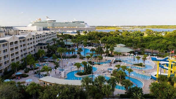 A resort with multiple swimming pools, a large cruise ship docked nearby, and lush greenery. - 2BR Villa at Holiday Inn Club Vacations Cape Canaveral Beach Resort (Cape Canaveral)