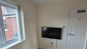 Ein Schlafzimmer mit Bett, Wandfernseher, Heizkörper, Fenster und Tür mit einem Schild.