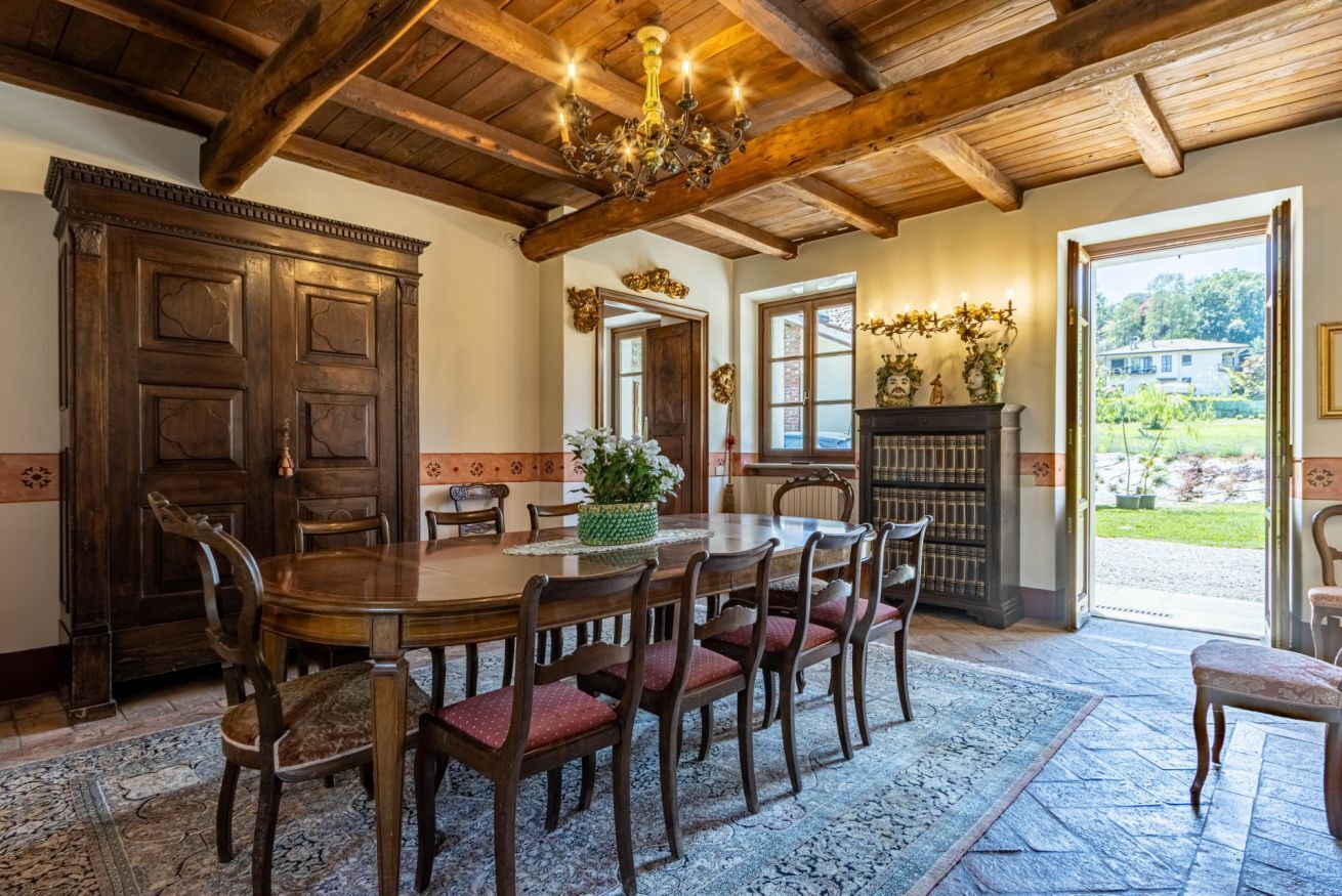 A dining area with a wooden table and chairs, a chandelier, and a view of the outdoors.