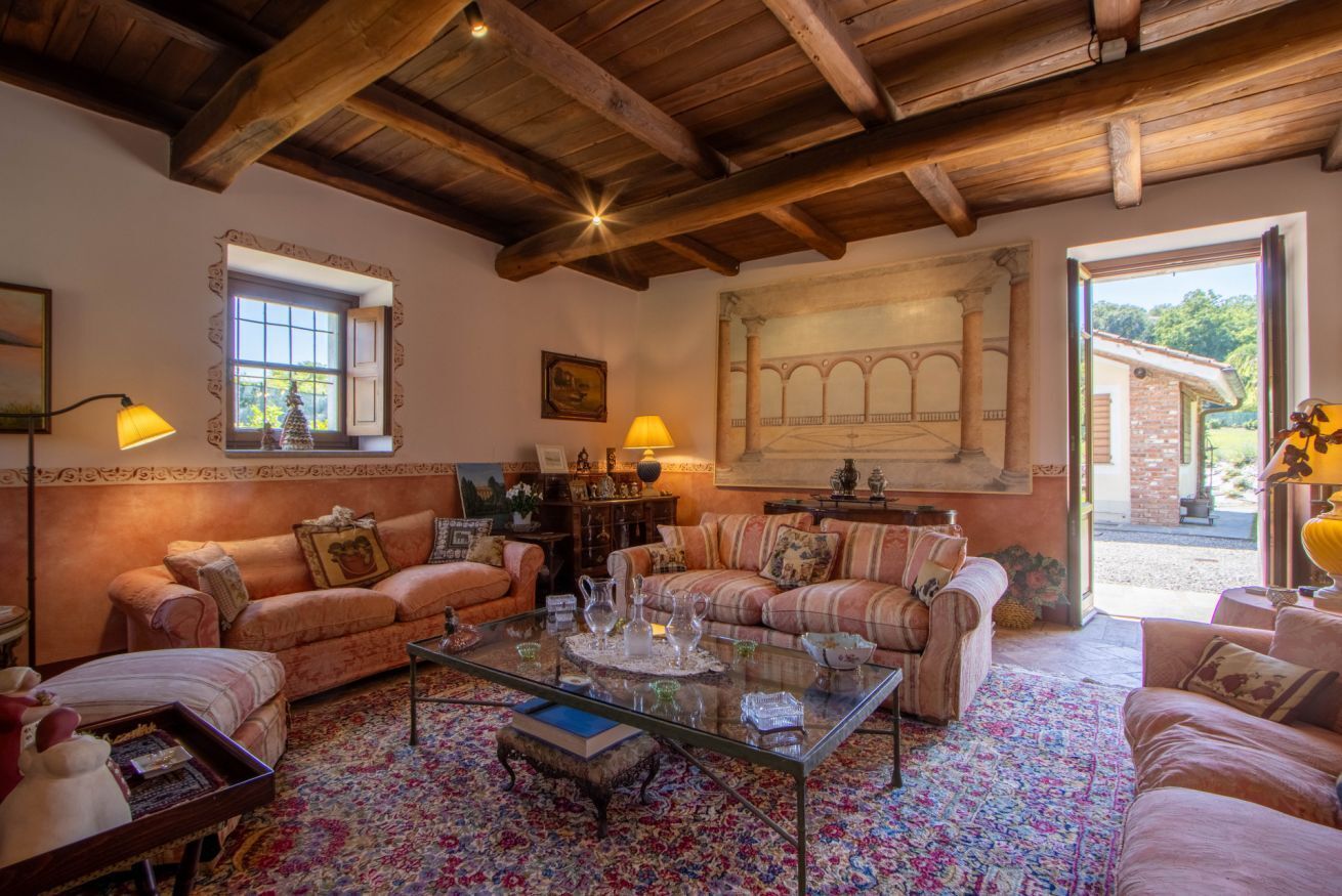 A cozy living room with a high wooden ceiling, two sofas, a glass coffee table, and a large window with a view.