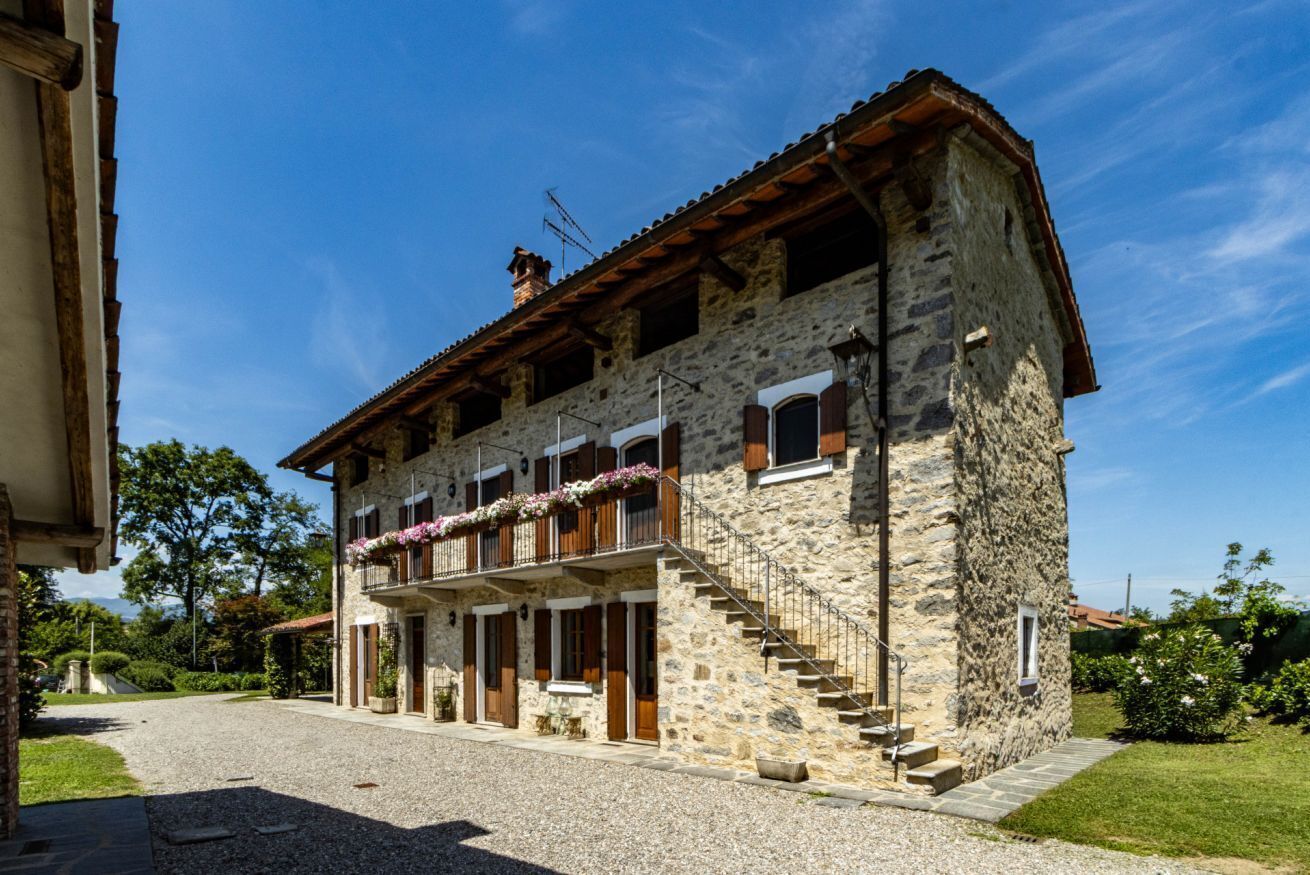 A stone building with a balcony, a staircase, and a gravel driveway.