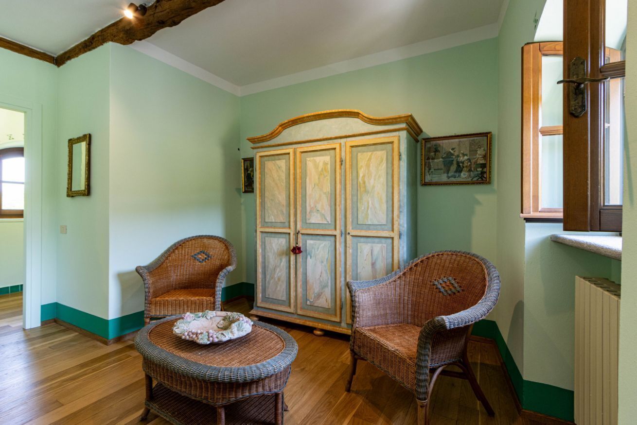 Een kamer met twee rieten stoelen, een tafeltje en een kast met decoratieve bovenkant.