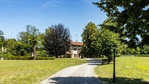 A gravel path leading to a building with a red roof, surrounded by greenery and trees. - Welcome to Villa Harmonia, a magnificent historic residence that has been carefully restored to preserve all the authentic charm of traditional Piedmontese farmhouses, combining elegance, comfort, and a timeless atmosphere.Nestled within more than 10,000 (Dormelletto)