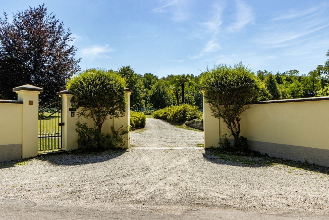 Una strada sterrata che conduce a un ingresso con cancello, sotto un cielo sereno.