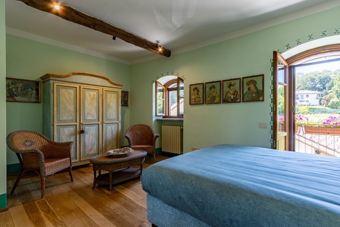 Una stanza con un letto, due poltrone in vimini, un tavolino, un armadio e una finestra vista verde.