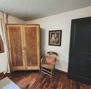 A room with a wooden wardrobe, a wicker chair with a cushion, a framed picture on the wall, and a dark door. - Tranquil organic microfarm with farm animals & AC in charming Battle Ground (Battle Ground)
