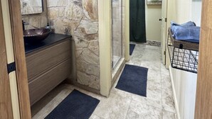 Un baño con pared de piedra, lavamanos, ducha y perchero para toallas.