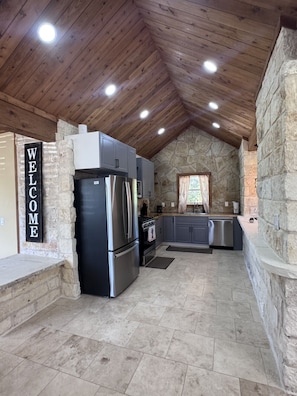 A kitchen with stone walls, a welcome sign, and modern appliances. - The Lodge at Ruby Ranch Getaways (Buda)
