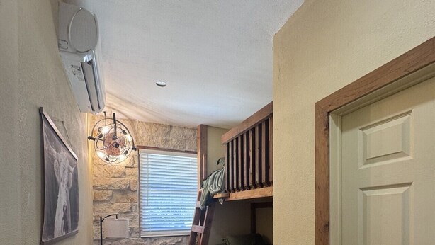 Una habitación pequeña con literas, una escalera, una mesita y un aire acondicionado instalado en la pared.