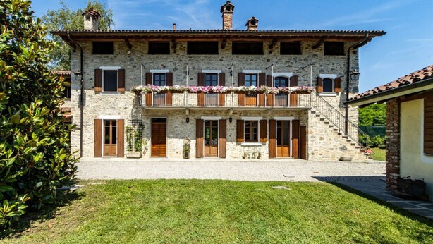 Un bâtiment en pierre de deux étages, doté d’un balcon, d’un escalier et d’une pelouse bien entretenue.