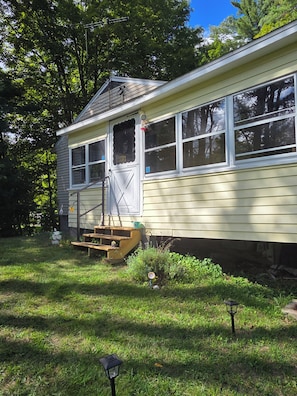 A single-story house with a front porch, a small set of steps, and a visible door. - 1950's Lake George house ranch trail & brook 3 bedroom 6 beds in Hague (Hague)