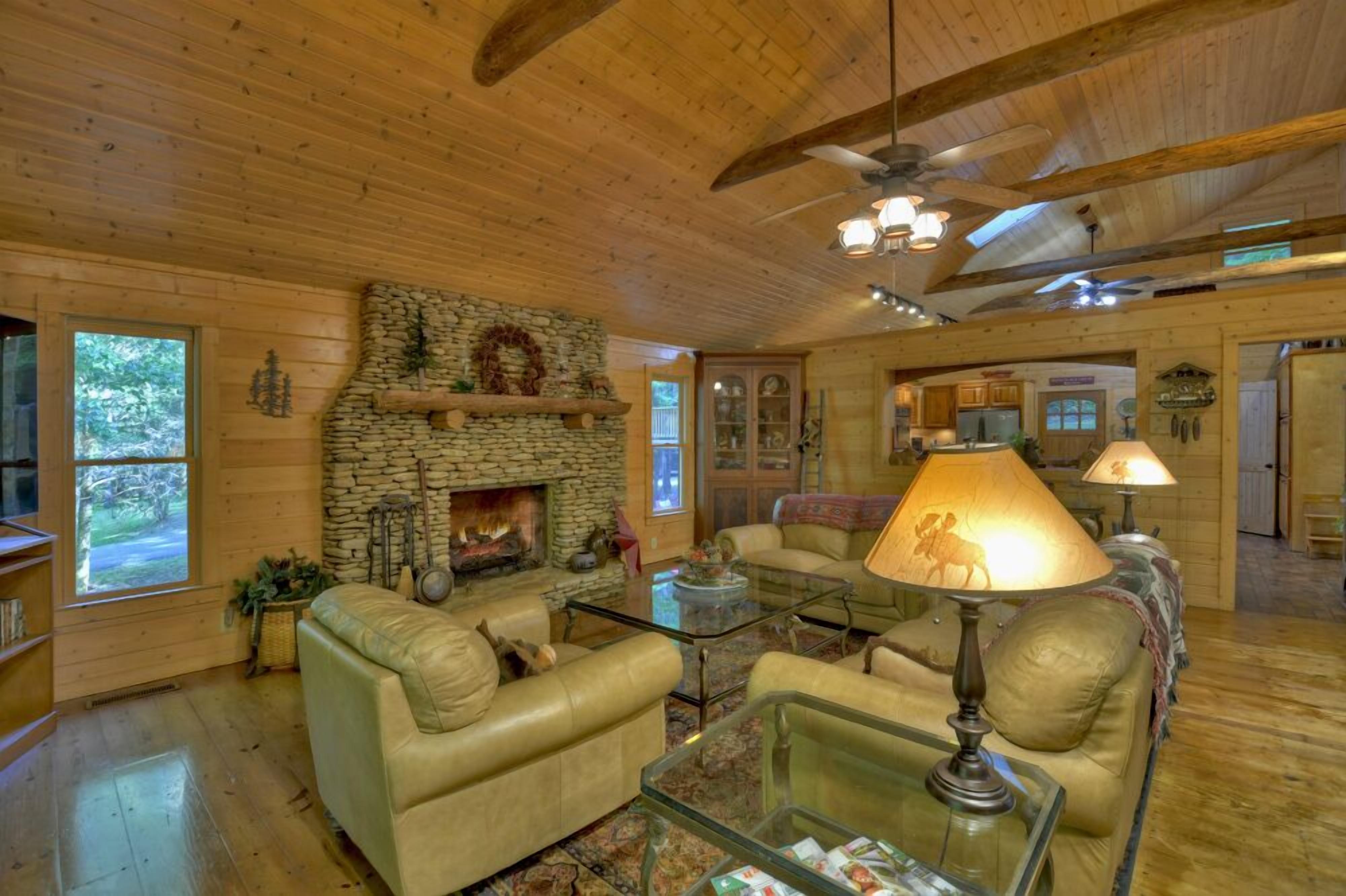 A cozy cabin interior with a stone fireplace, leather sofas, and a ceiling fan.