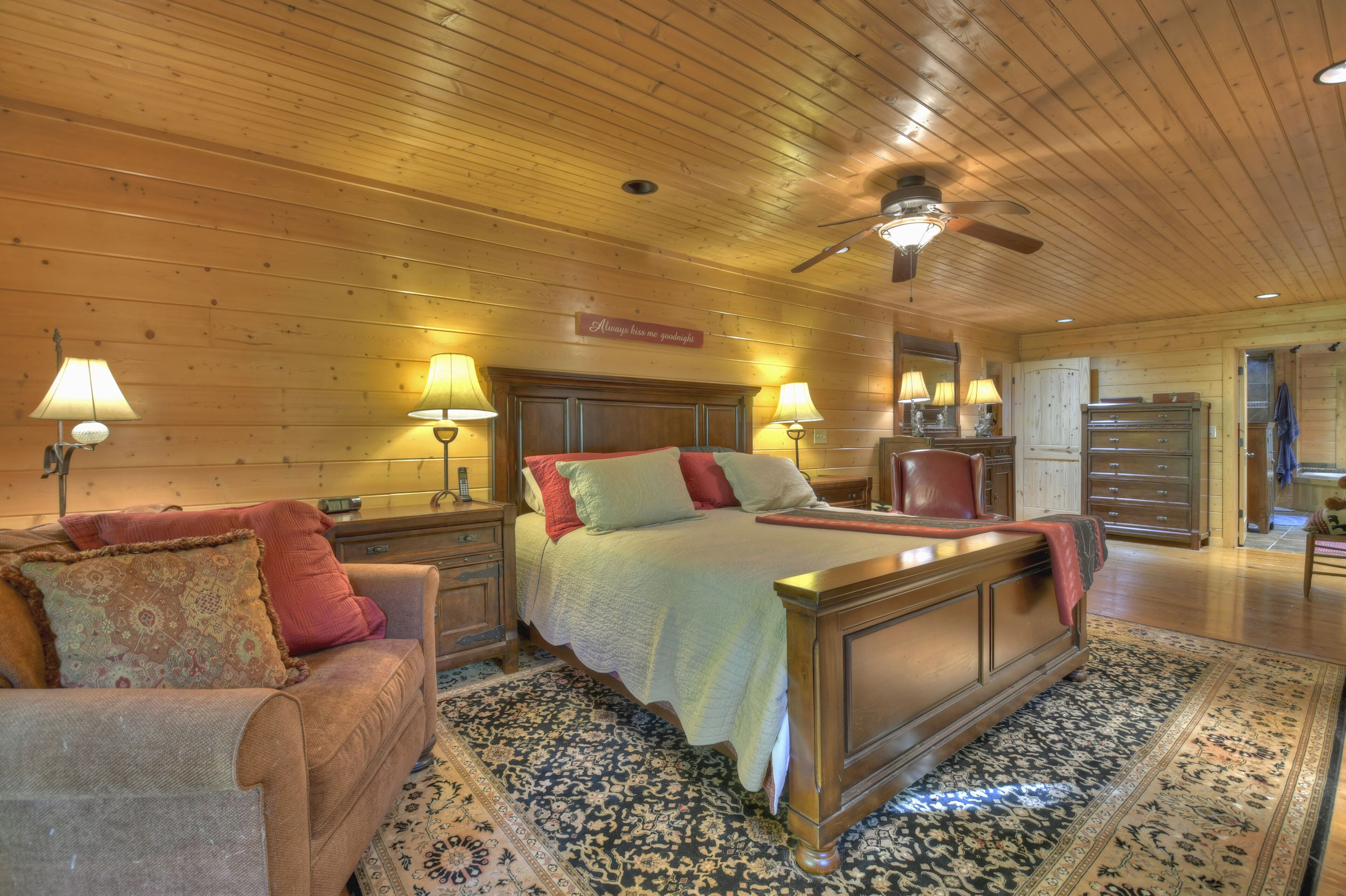 A bedroom with a large bed, wooden ceiling, and a ceiling fan.