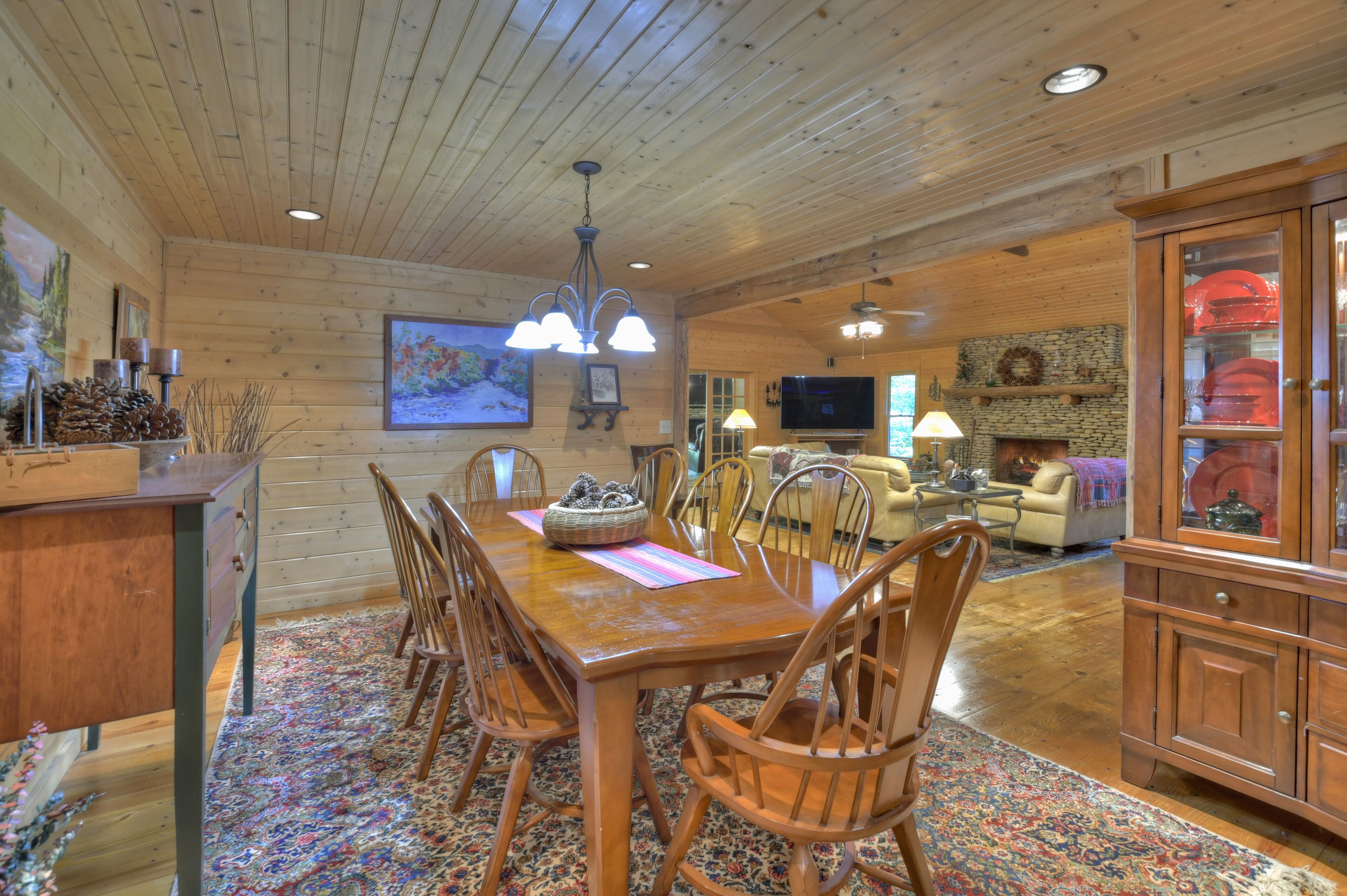 A wooden interior with a dining table, chairs, a television, and a fireplace.