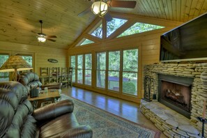 A spacious living room with a stone fireplace, leather sofas, and large windows offering a view of the outdoors. - Time Out On The Toccoa | Blue Ridge, GA (Blue Ridge)