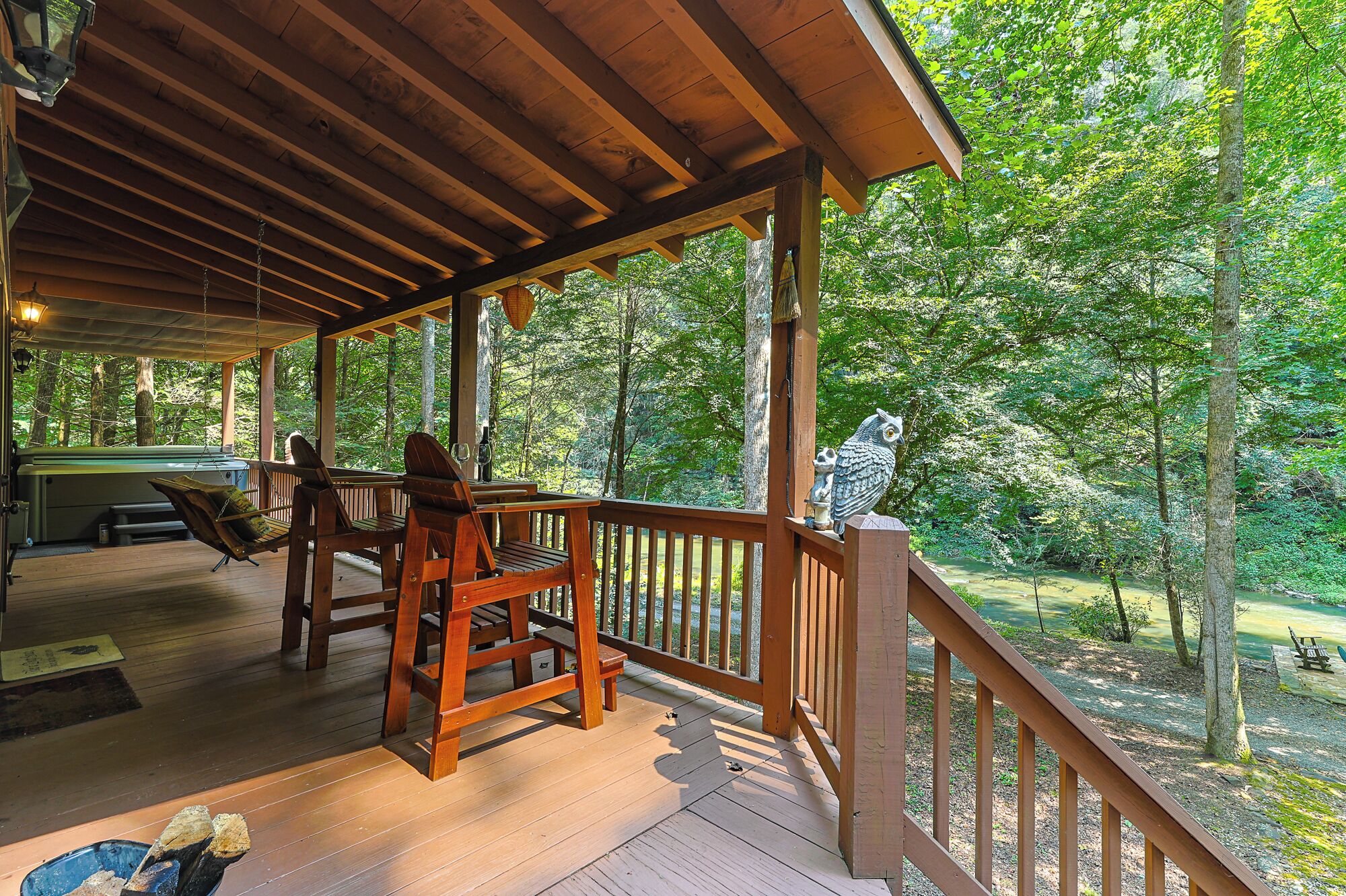 A wooden deck with outdoor seating, a hot tub, and a view of a forested area.
