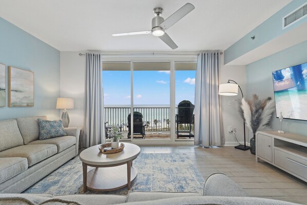 Un salon doté d’un ventilateur de plafond, d’un canapé, d’une table basse et offrant une vue sur la plage grâce à de grandes portes coulissantes.