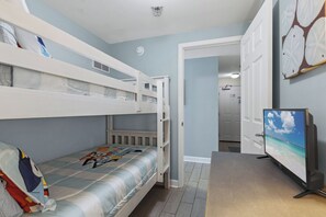 Une chambre avec des lits superposés, une télévision et une porte donnant sur une autre pièce.