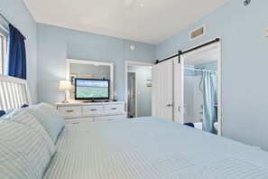 A bedroom with a bed, a television, a dresser, and a bathroom with a shower curtain. - Shores of Panama 721~Sleeps 8 (Panama City Beach)