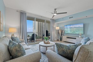 Ein modernes Wohnzimmer mit einer Sofagarnitur, einem Couchtisch, einem Fernseher und einem Balkon mit Blick auf ein Hochhaus.