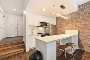A modern kitchen with white cabinetry, a brick accent wall, and a bar area with stools. - Modern Downtown Montreal Loft • 2-Bedroom • Steps to Old Port (Montreal)