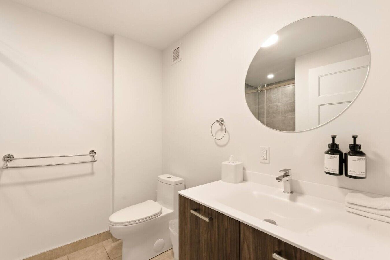 A modern bathroom with a toilet, bidet, sink, mirror, and two bottles of hand soap.