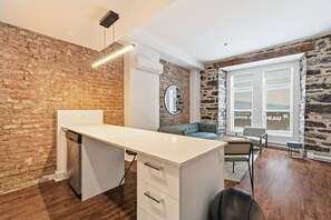 Une pièce moderne avec un mur en briques, un bureau blanc avec des tiroirs, un canapé bleu et une grande fenêtre donnant sur un beau paysage.