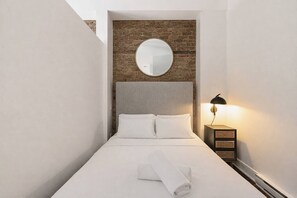 Ein Hotelzimmer mit einer Wand aus Backsteinen, einem runden Spiegel, einem Bett mit weißer Bettwäsche und einer Nachttischlampe.
