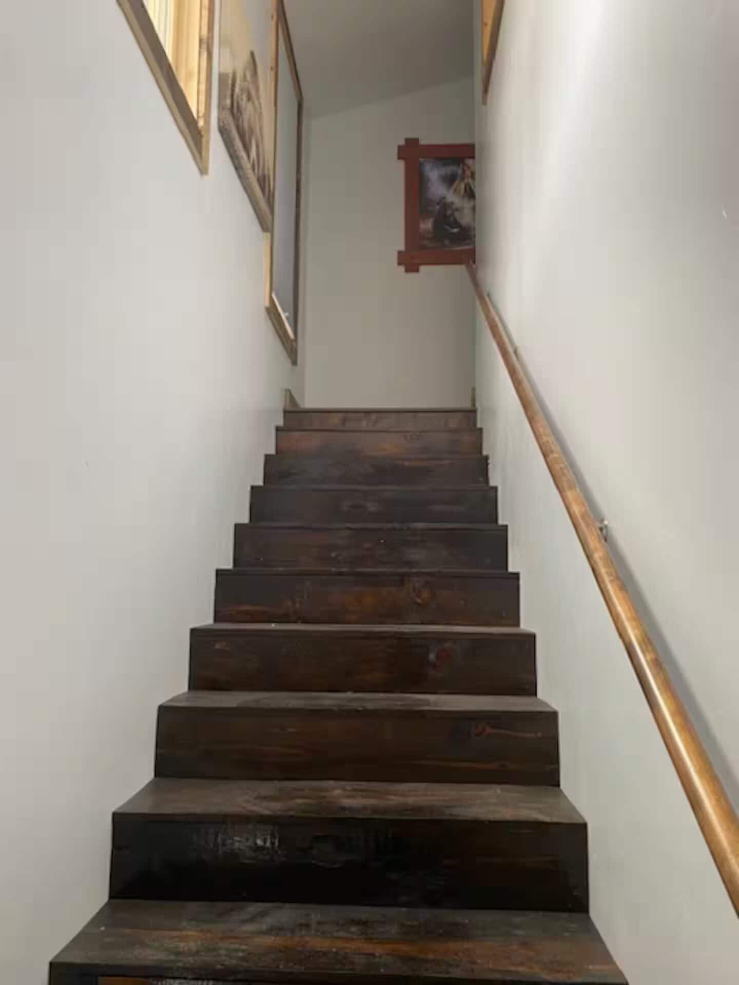 A wooden staircase with a handrail, leading to a landing with framed pictures on the walls.