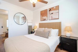 Ein Schlafzimmer mit einem Bett, Nachttischen, einem runden Spiegel und abstrakten Wandbildern.
