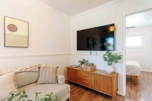 Een woonkamer met een bank, een houten kast, een aan de muur bevestigde televisie en een raam.