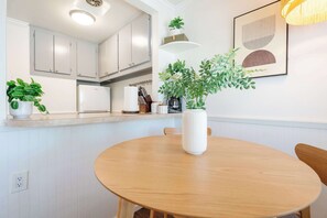 Eine Küche mit weißen Schränken, einem runden Holztisch und einem Blumentopf auf der Arbeitsplatte.