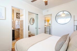 Een slaapkamer met een bed, een ronde spiegel, een plafondventilator en uitzicht op de badkamer.